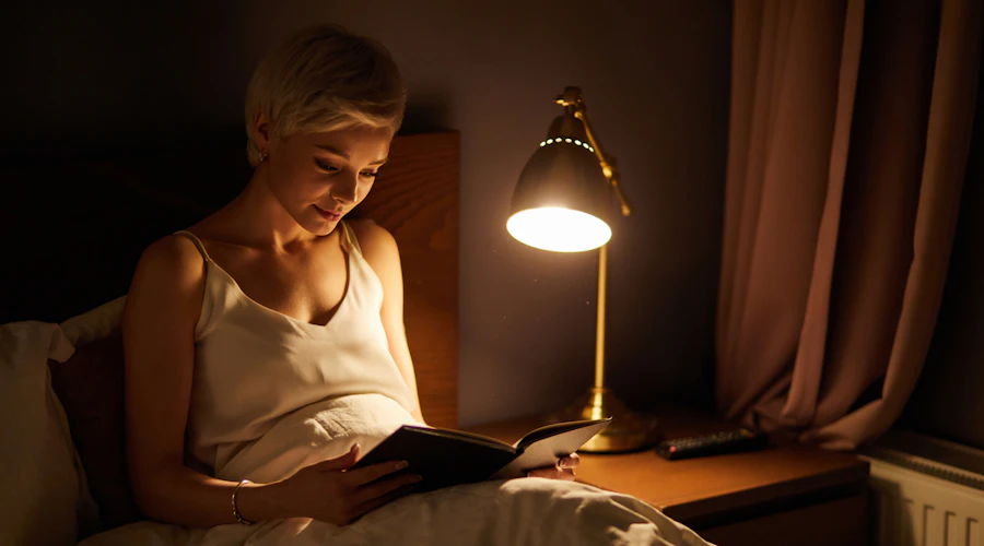 Woman reading in bed by lamp light.