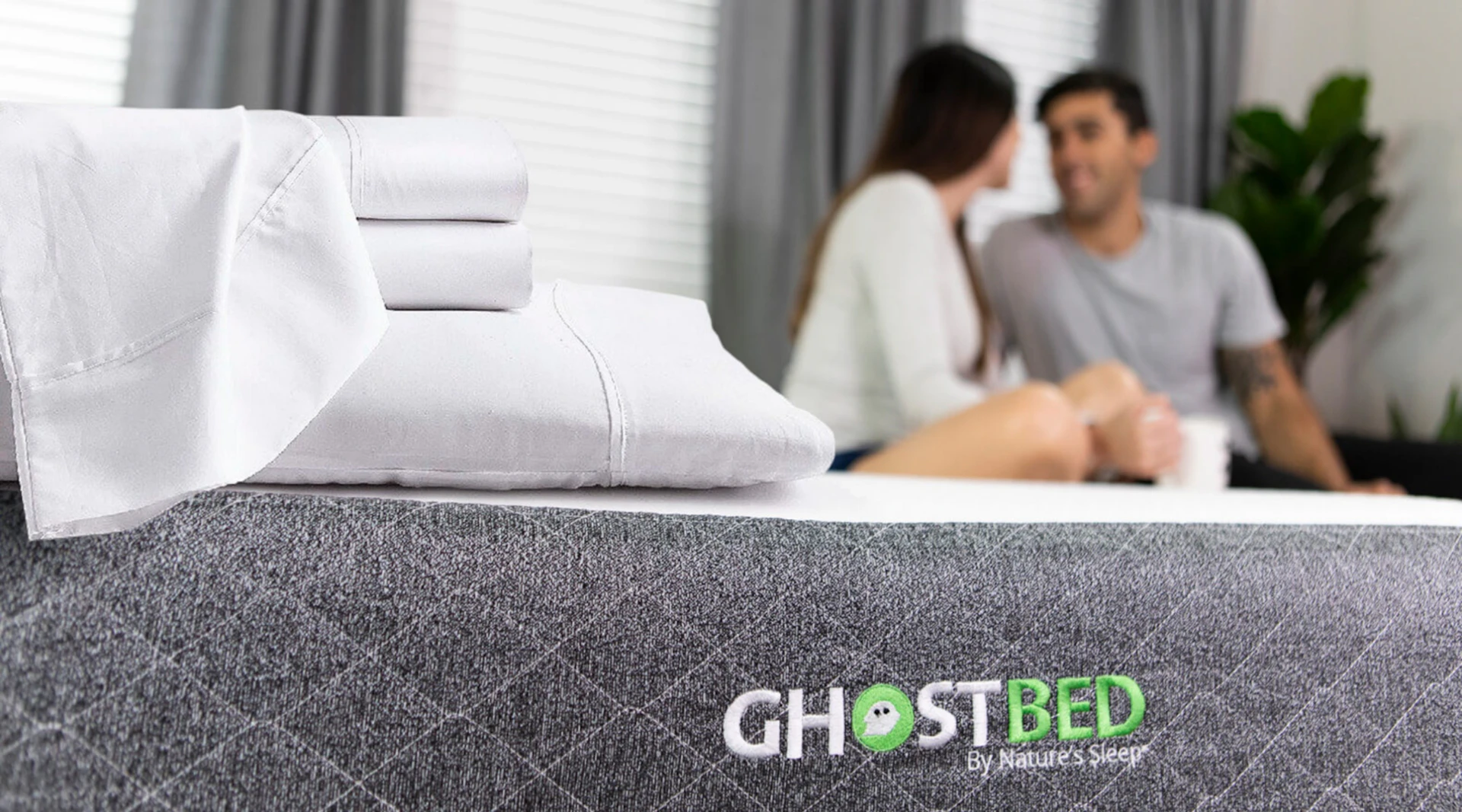 A couple relaxes on a GhostBed Adjustable Base, with bed sheets folded on the corner.