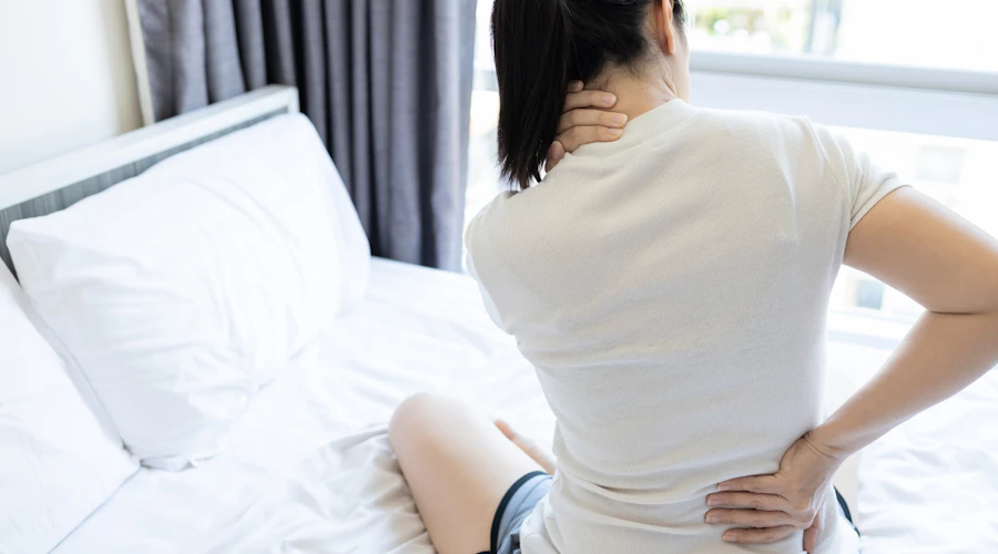Woman sitting up with back and neck pain after sleeping on a bad pillow.