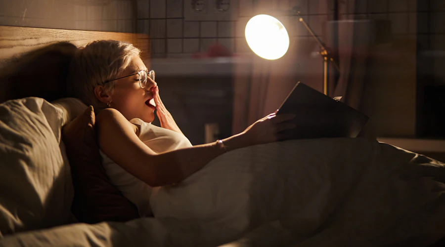 Femme lisant un livre au lit et bâillant.