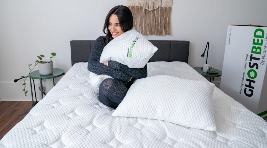 Woman in pajamas holds GhostPillow on bed.