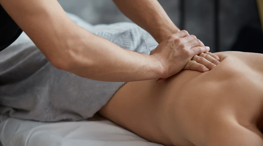 Un homme se fait masser sur une table de massage sous une couverture grise.