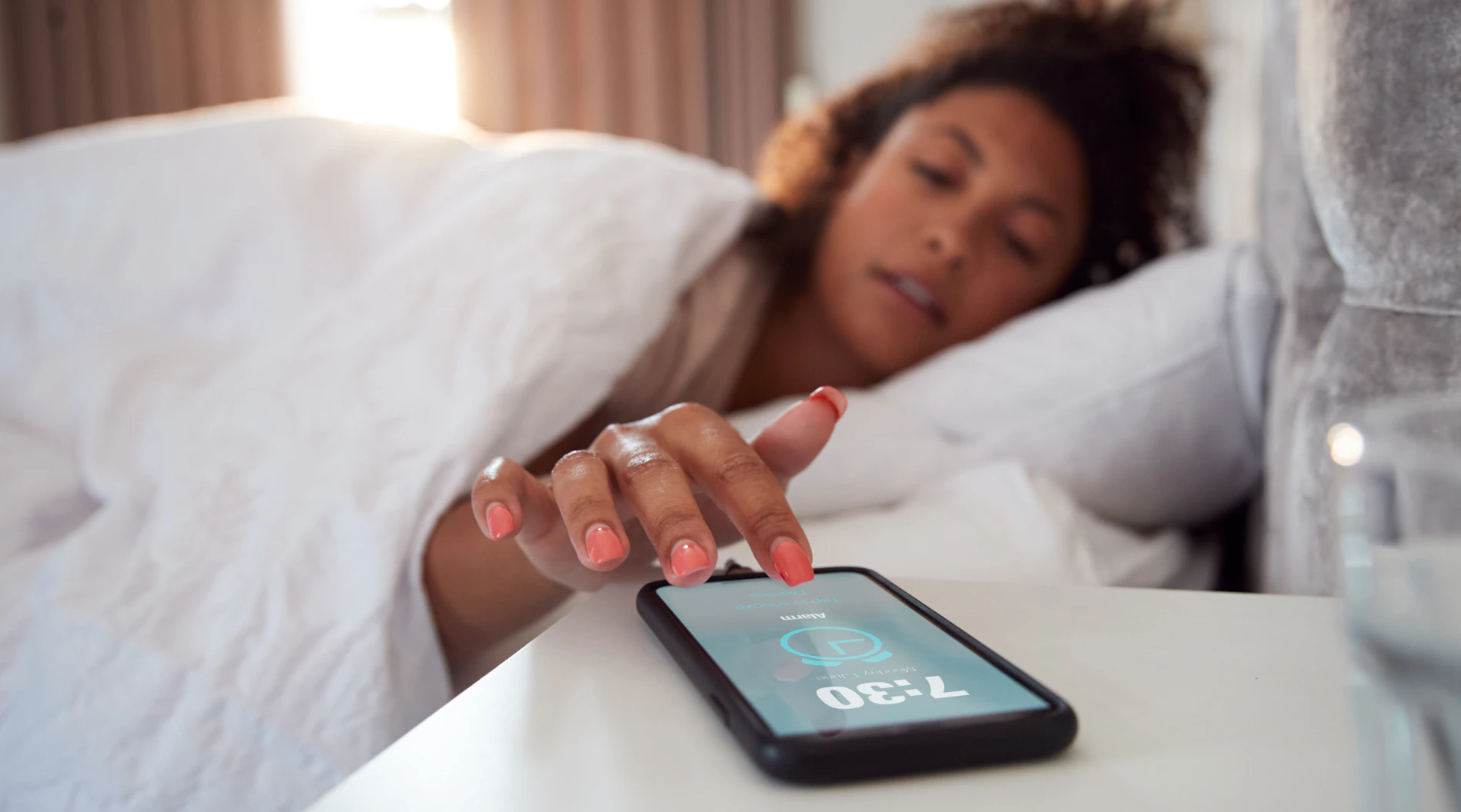 Woman in bed, turning off alarm clock on phone.