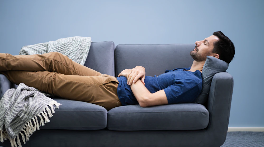Un homme fait la sieste sur un canapé en levant les pieds.