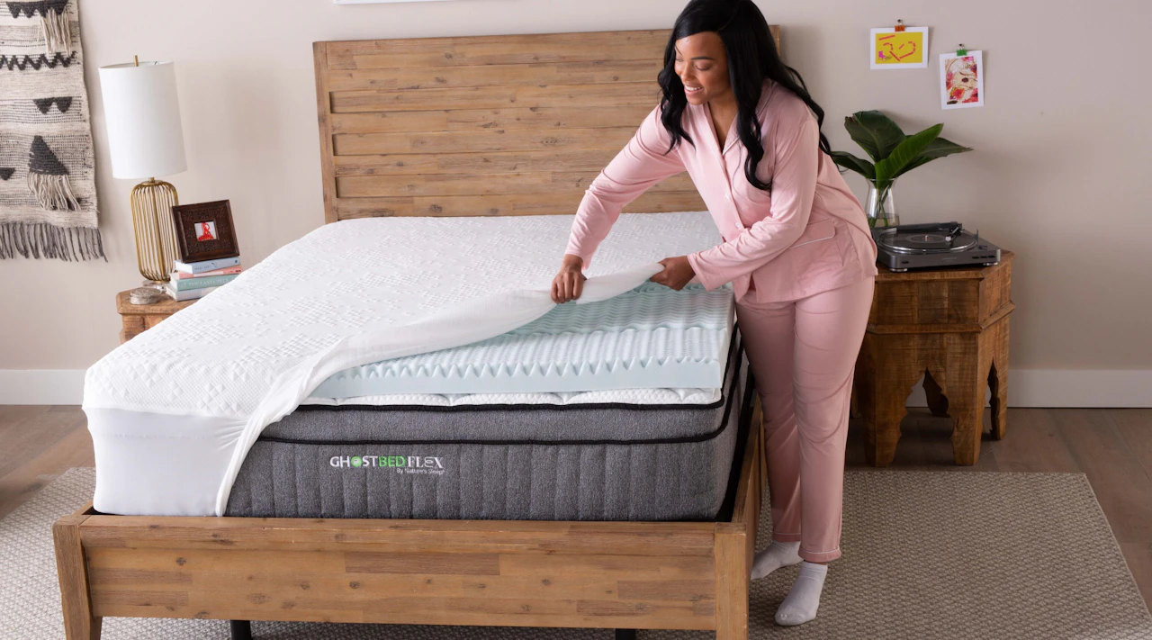 A woman places the GhostBed 3” Memory Foam Topper on her mattress for extra pressure relief.