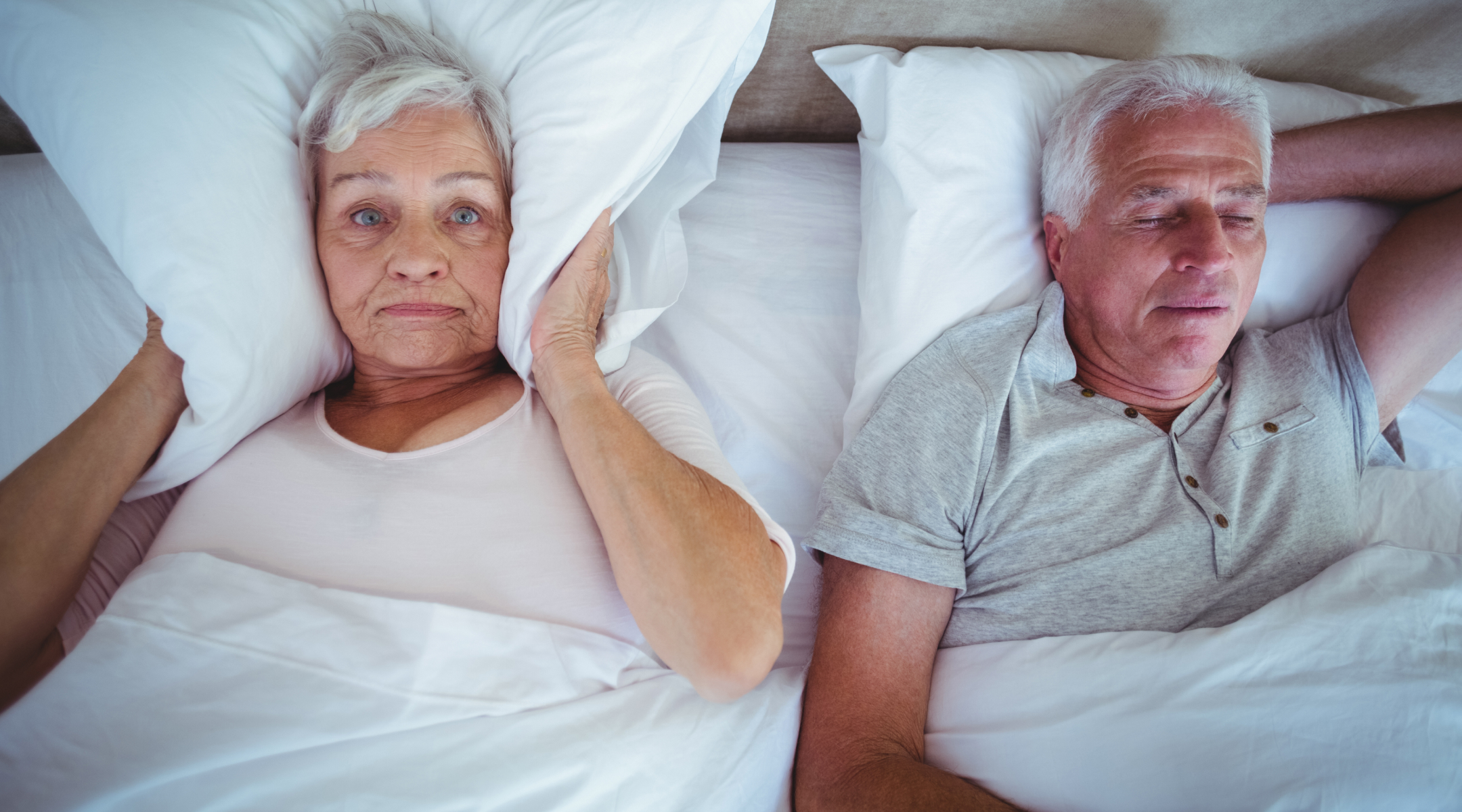 A woman holds a pillow over her ears, trying to sleep while her husband snores.